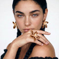 Woman wearing gold floral earrings and ring on a white background