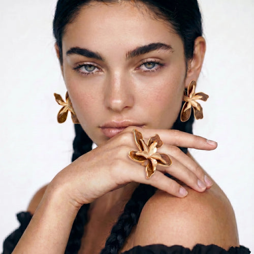 Woman wearing gold floral earrings and ring on a white background