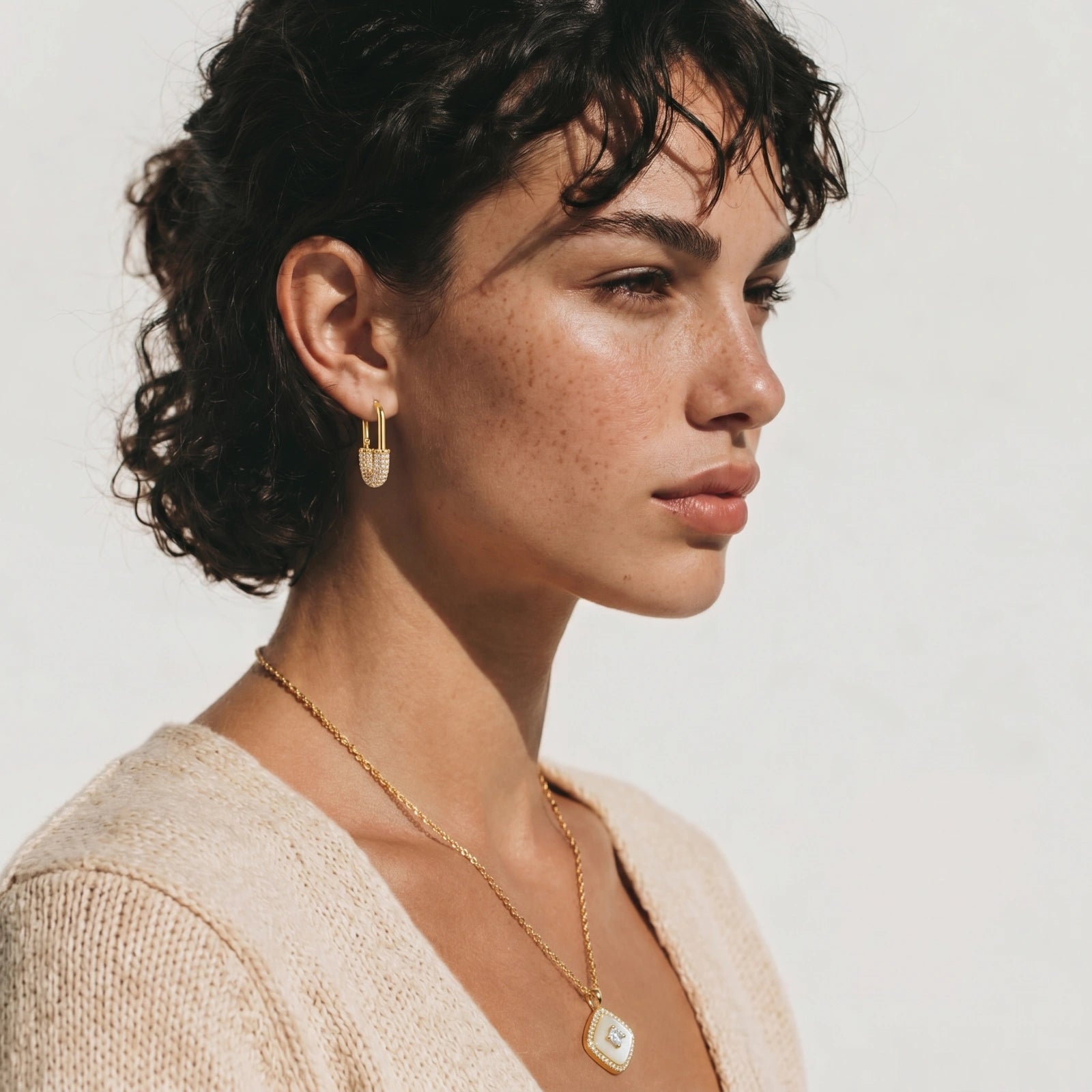 Woman wearing gold earrings and necklace against a neutral background