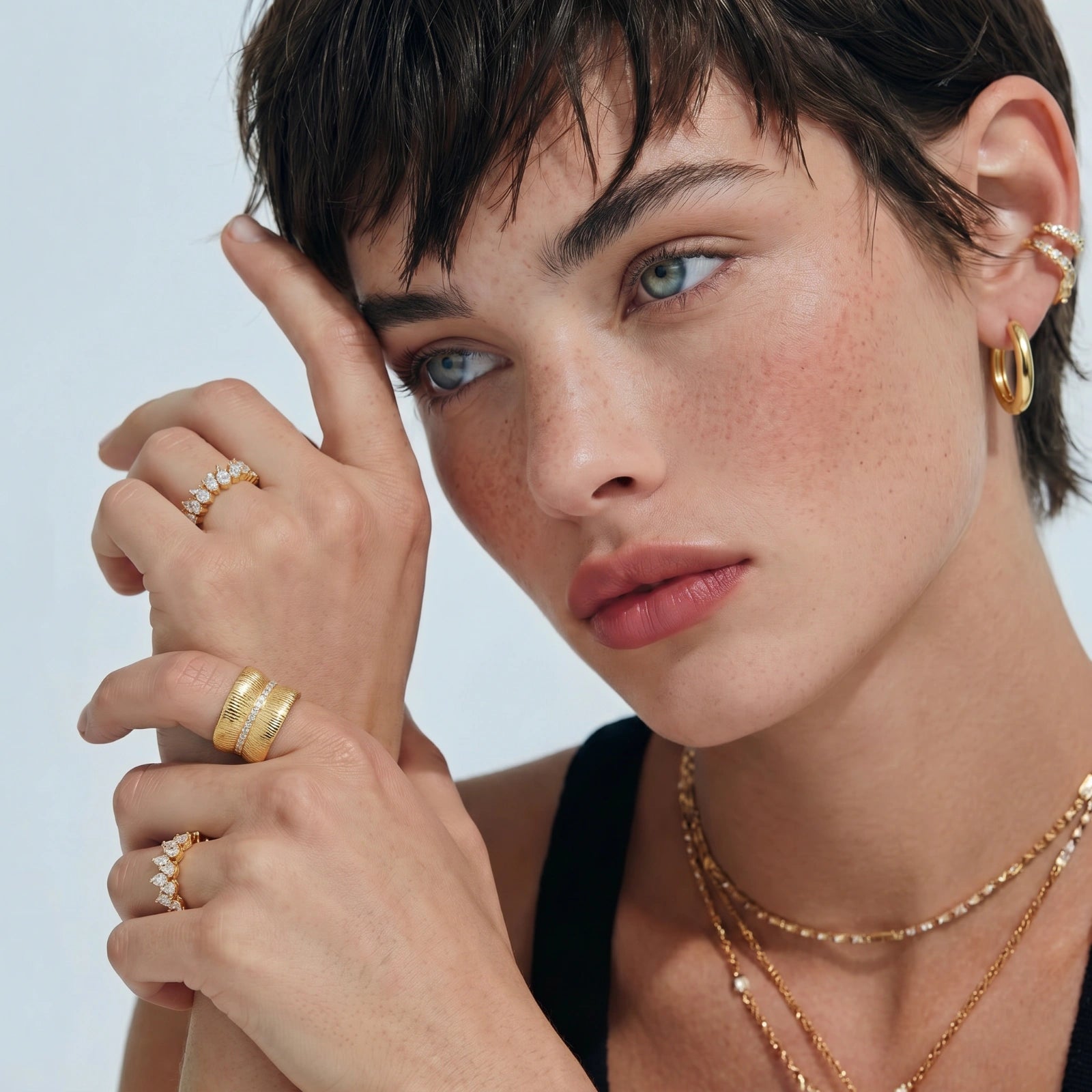 Woman wearing gold jewelry including rings and earrings against a light background