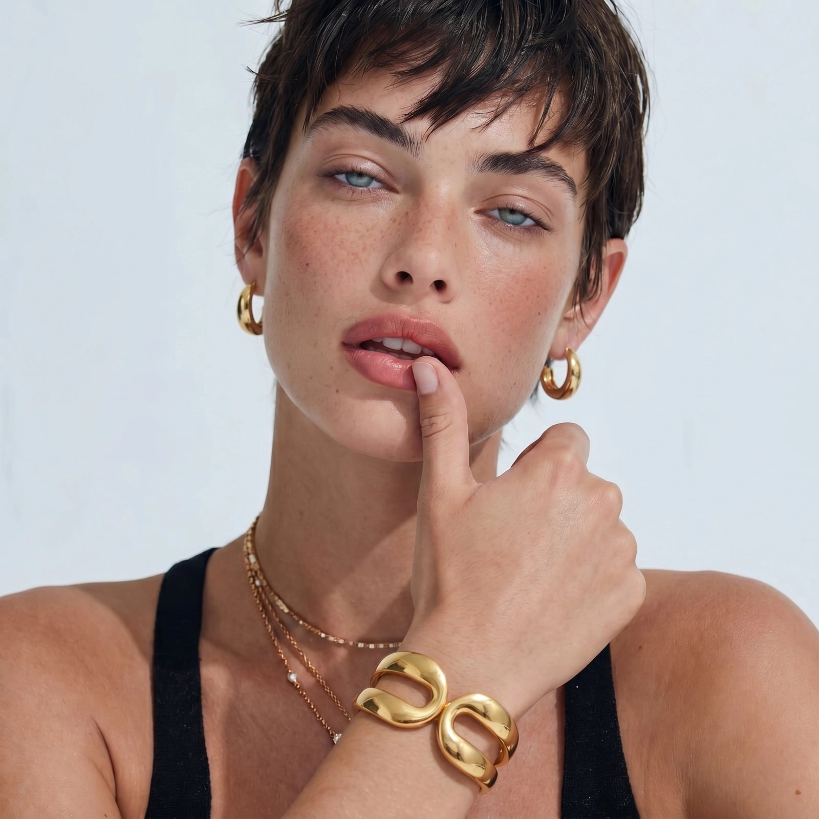 Woman wearing gold jewelry including earrings and a bracelet on a white background