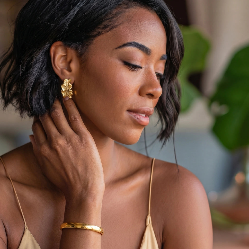Woman wearing gold earrings and bracelet, with a blurred natural background