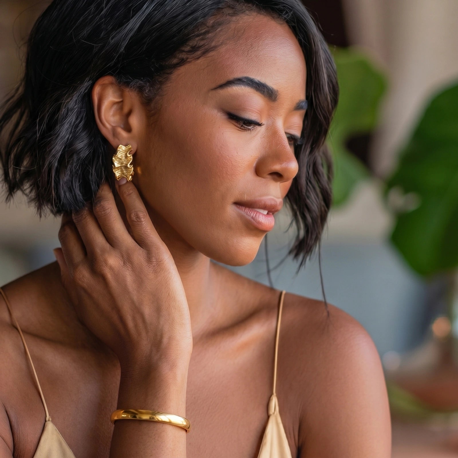Woman wearing gold earrings and bracelet, with a blurred natural background