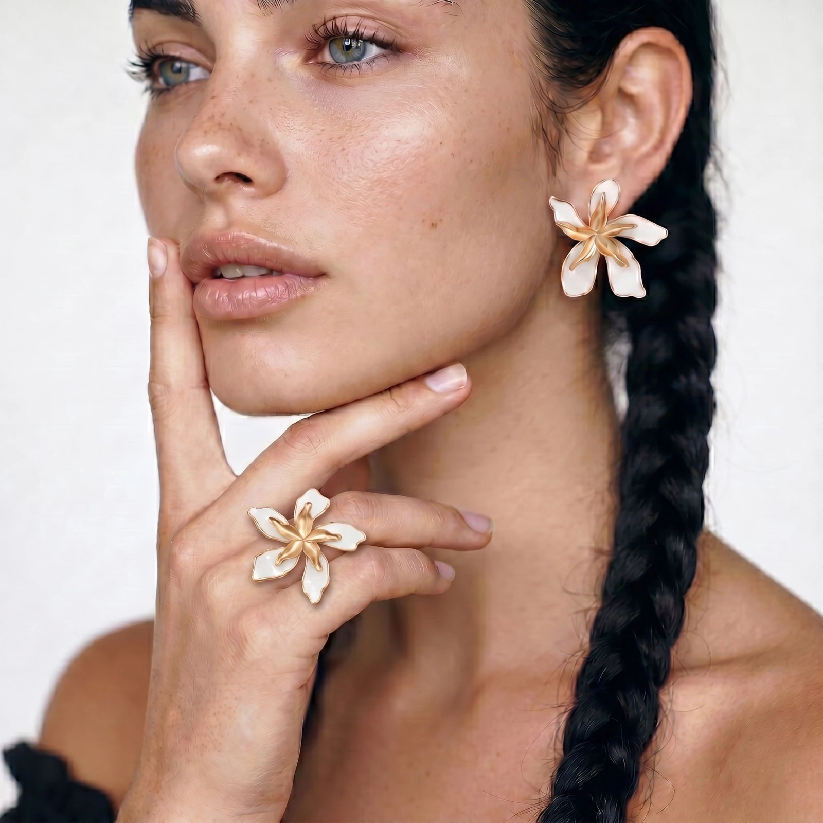 Woman with braided hair wearing floral earrings and a ring on a white background