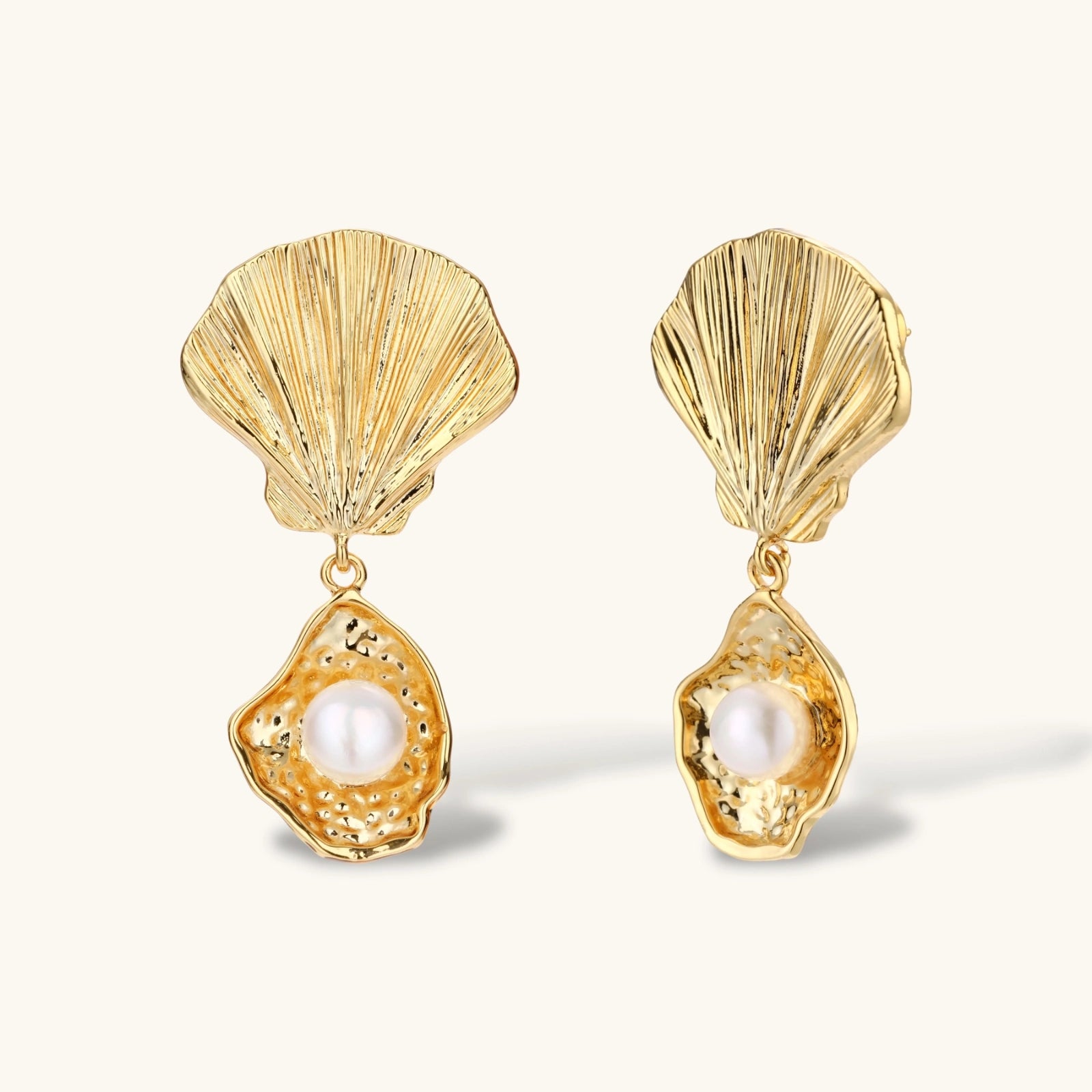 Gold shell-shaped earrings with pearl centers on a light beige background