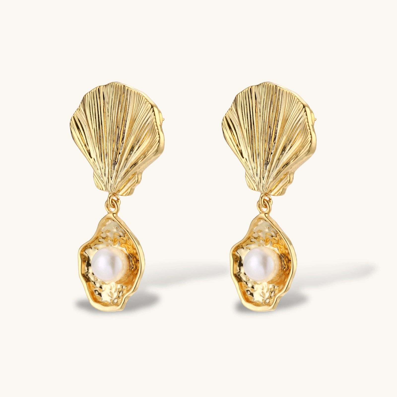 Gold shell-shaped earrings with pearl centers on a white background