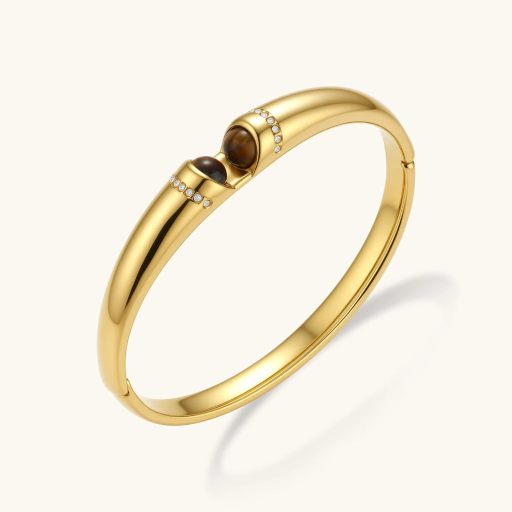 Gold bracelet with a central brown gemstone on a white background