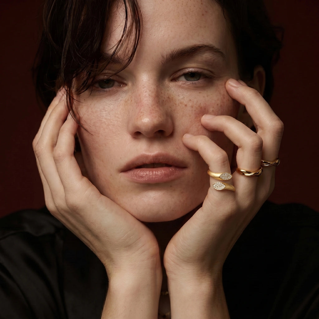 Woman with freckles wearing gold rings on a dark background