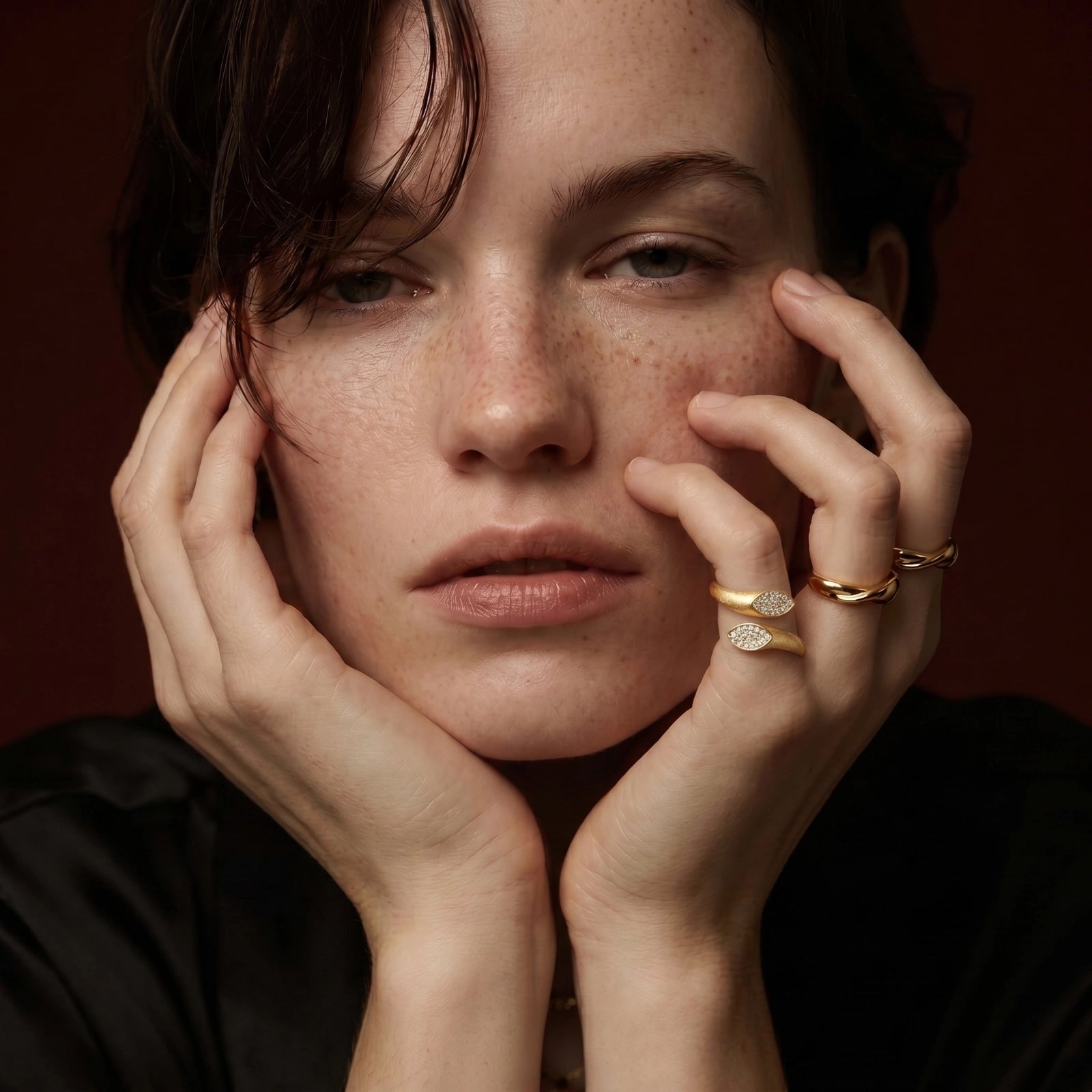 Woman with freckles wearing gold rings on a dark background